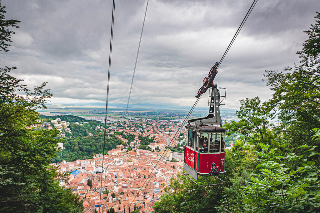 A red cable call filled with people going down from Tampa Mountain, in the background the city of Brasov